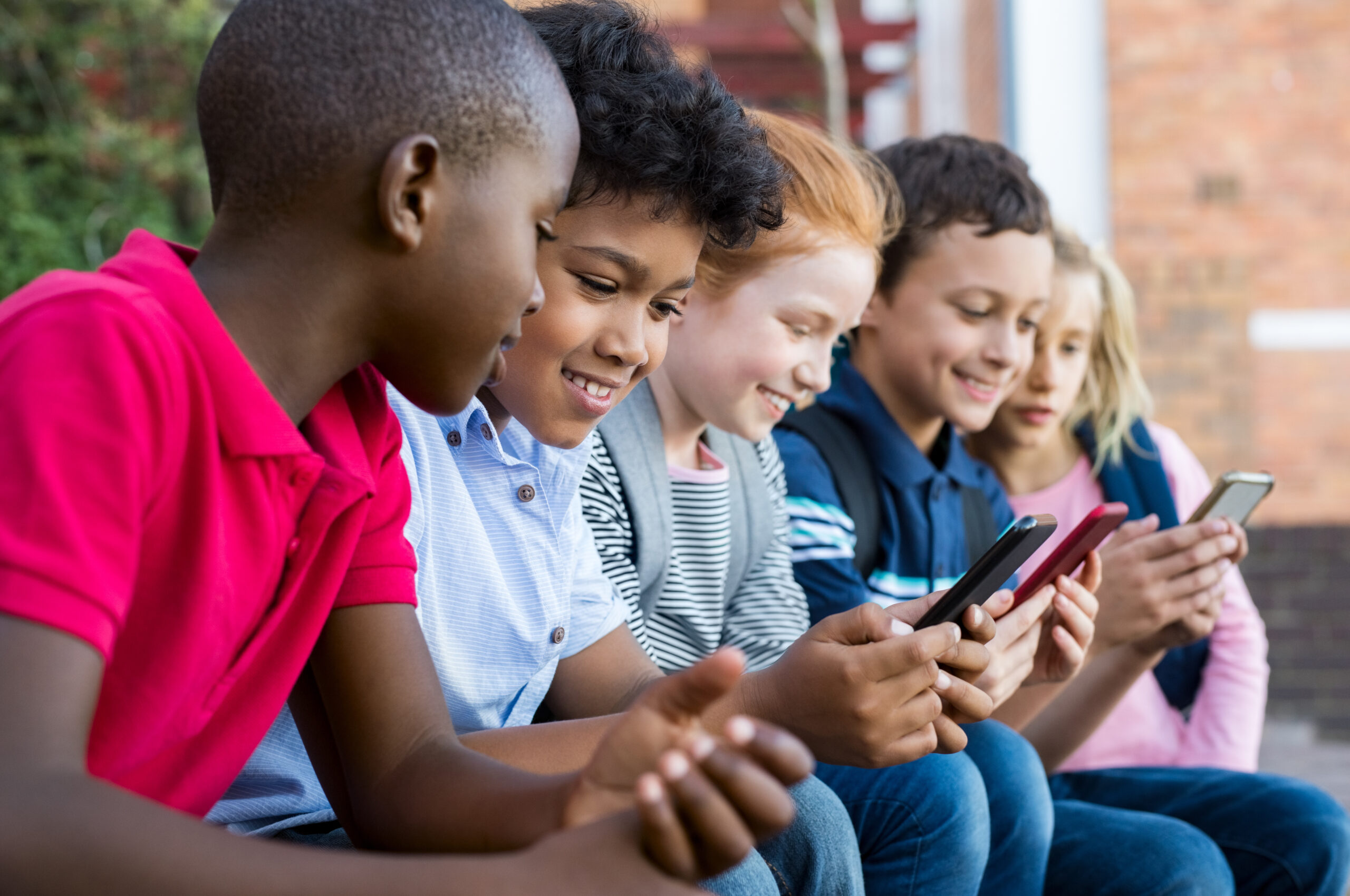 Children sitting together outside using their phones and smiling