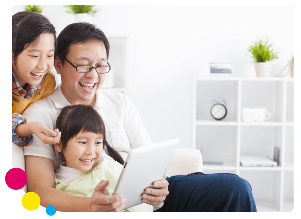 A father and his daughters learn English at home with Little Bridge on a tablet with colourful circles
