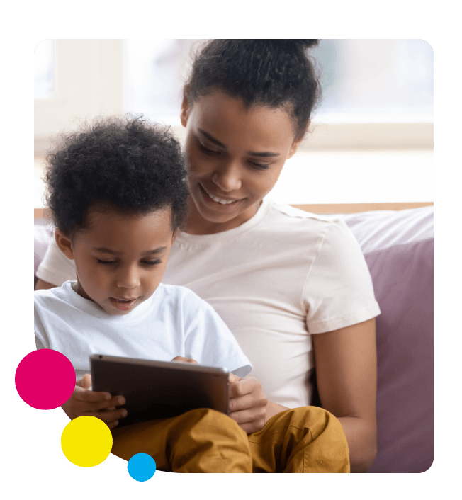 A mother and her young child sit on the sofa learn English with Little Bridge on a tablet with colourful circles