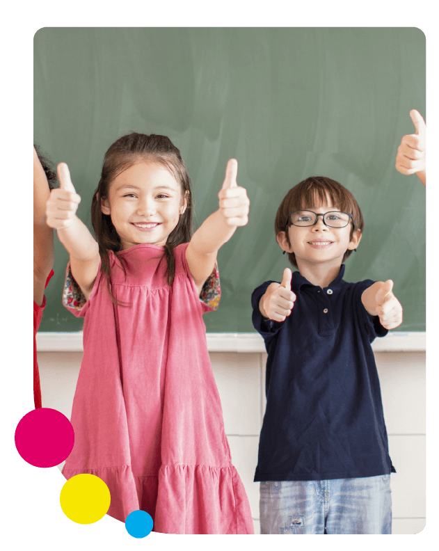 Two students in bright clothing standing in front of a chalk board with their thumbs up