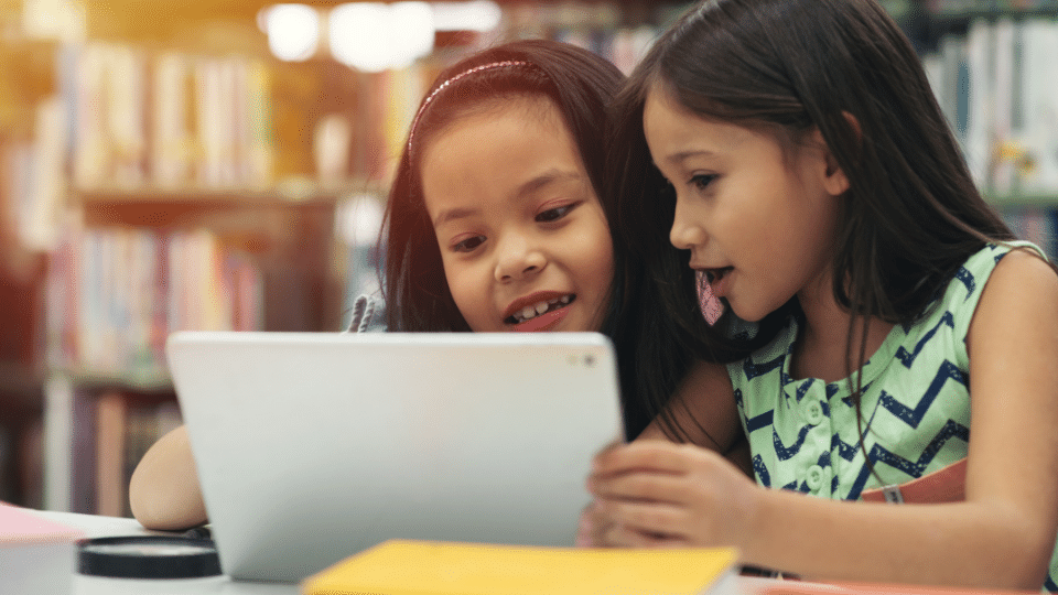 2 children learning English with Little Bridge on a tablet, looking excited